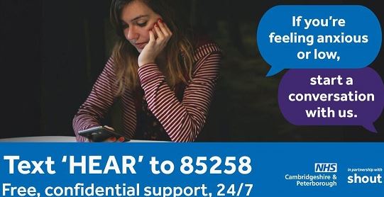 Woman using her phone in a dark room. Text bubbles say: If you're feeling anxious or low, start a conversation with us. White text on a blue banner reads: Text HEAR to 85258 Free confidential support 24/7. NHS Peterborough and Cambridgeshire, and in partnership with shout logos are on the bottom right corner.